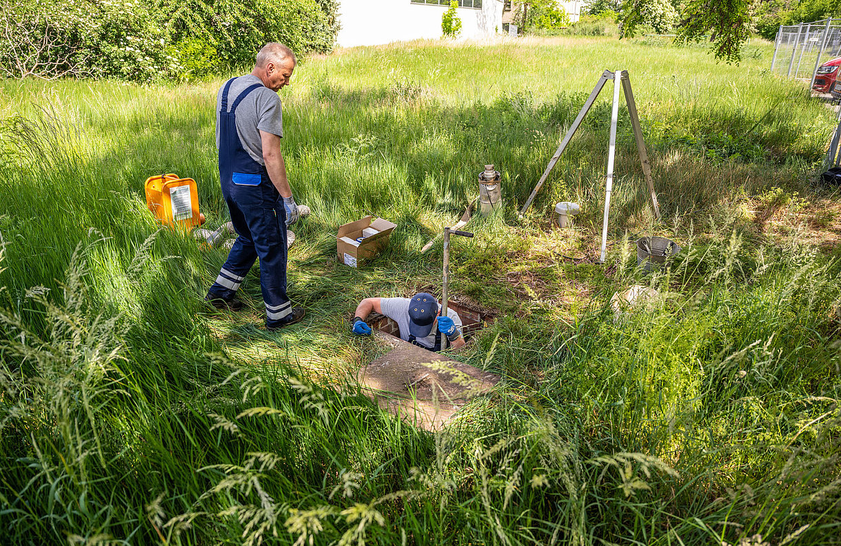 Zwei SWM Mitarbeiter aus dem Bereich Wasser steigen in einen Schacht zum Wechsel eines Großwasserzählers