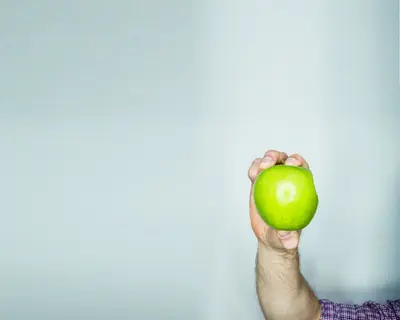 Ein Männerarm hält einen Apfel ins Bild.