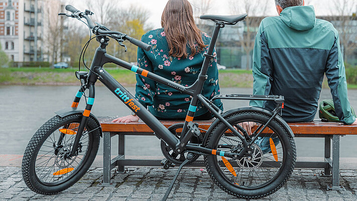 zwei Radfahrer:innen sitzen auf einer Bank, davor stehen zwei E-Bikes E.mil