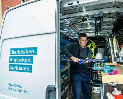 Azubi Anlagenmechaniker steht im SWM Firmenfahrzeug und arbeitet