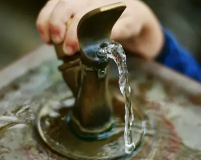 Eine Kinderhand bedient einen Trinkbrunnen aus dem frisches Wasser fließt.