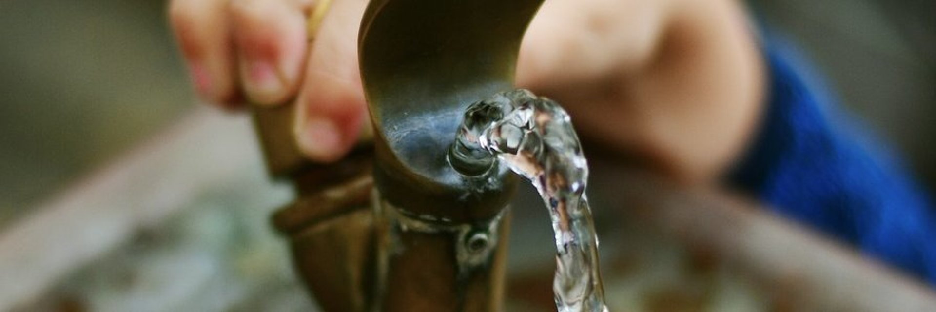 Eine Kinderhand bedient einen Trinkbrunnen aus dem frisches Wasser fließt.