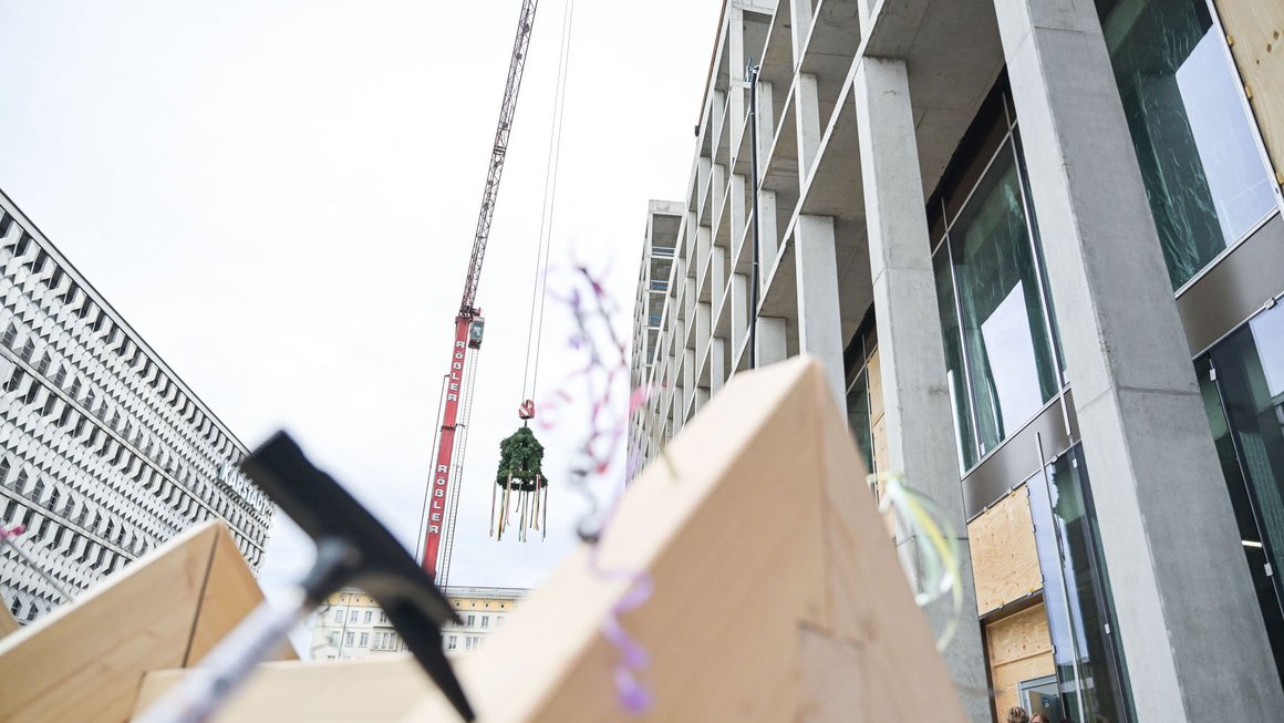 Richtkranz am Kran vor dem Rohbau des neuen Blauen Bocks im Hintergrund, Hammer im Vordergrund