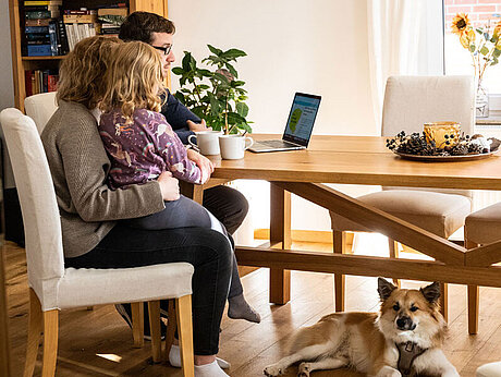 Familie mit Hund sitzt am Tisch und arbeitet gemeinsam am PC