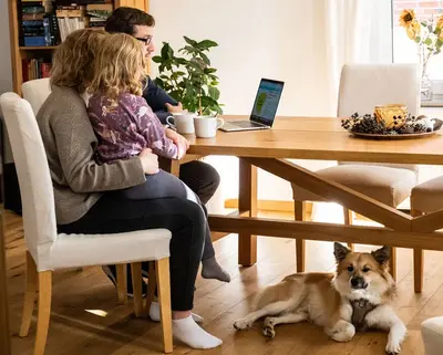 Familie mit Hund sitzt am Tisch und arbeitet gemeinsam am PC