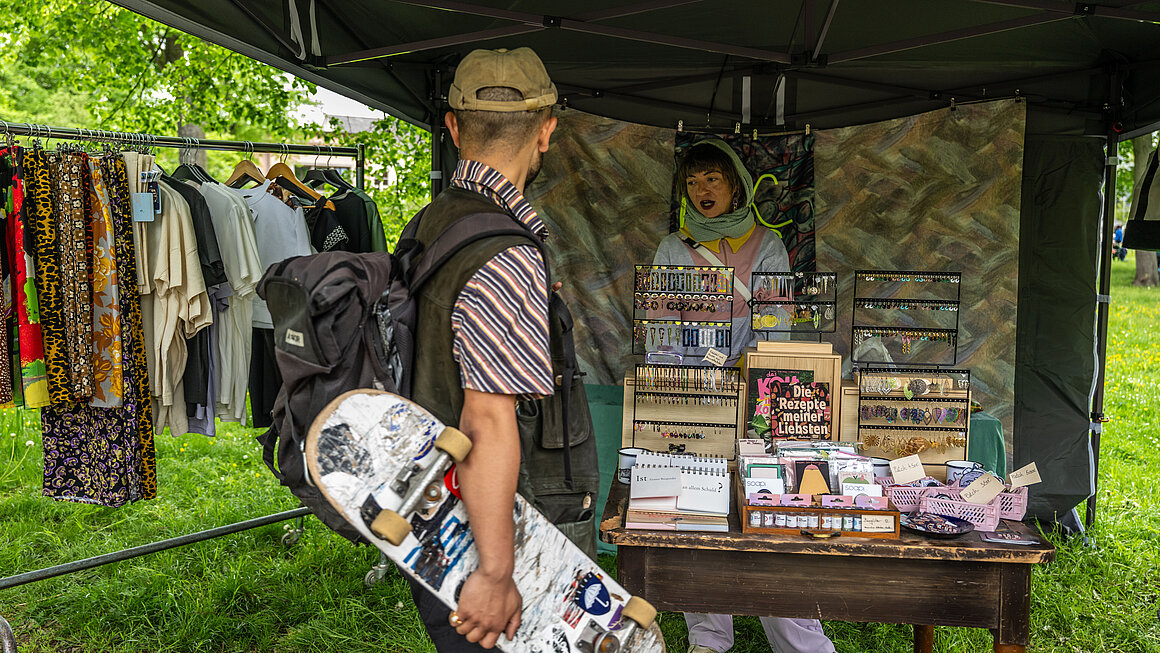 Mann mit Skateboard in der Hand sieht sich Stand mit Schmuck an