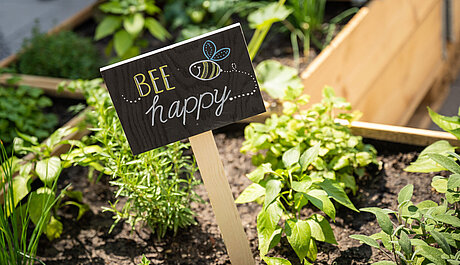 Schild "bee happy" in Nachbars Garten
