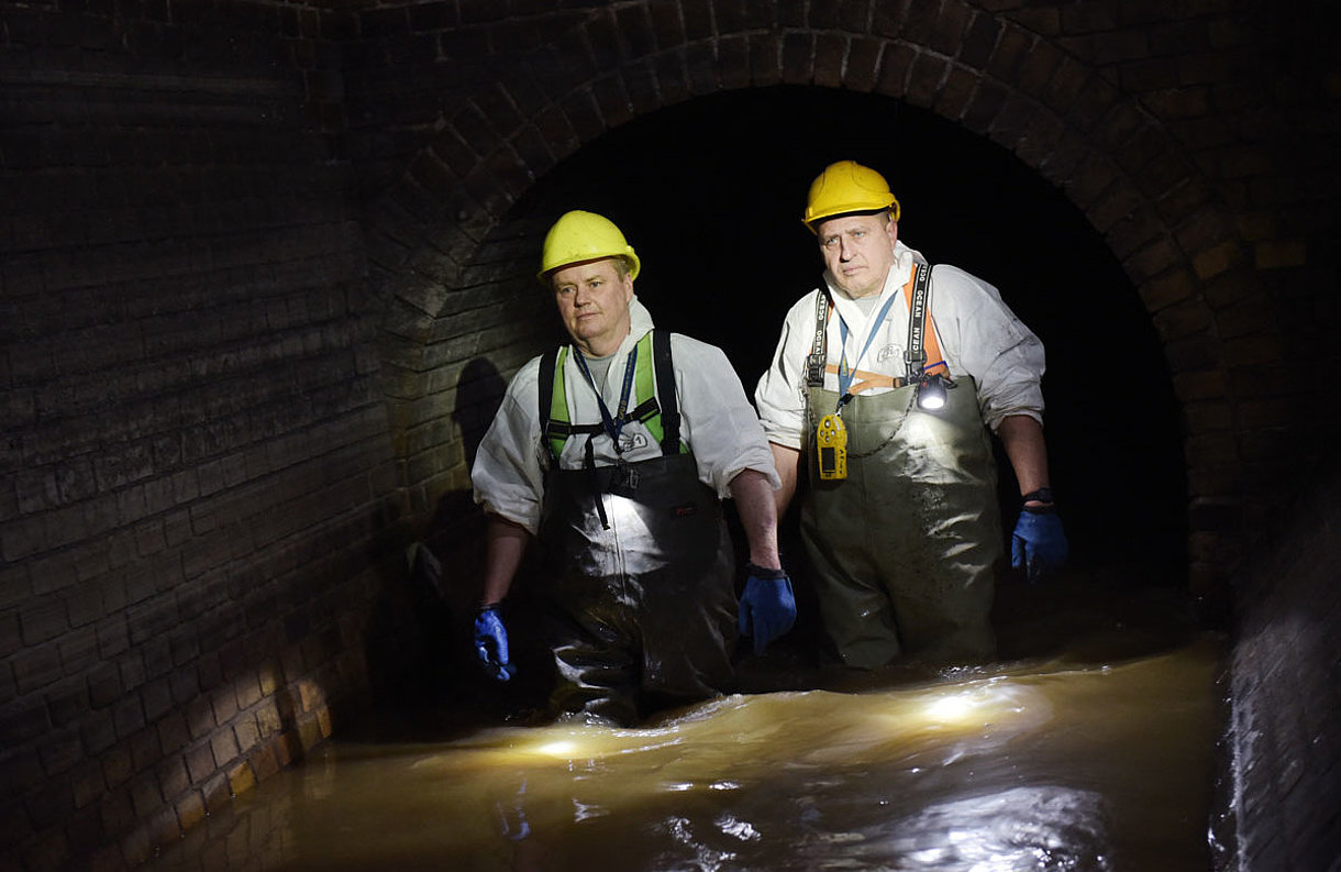 Zwei Mitarbeiter von SWM aus dem Bereich Abwasser gehen durch Abwasser im Kanal