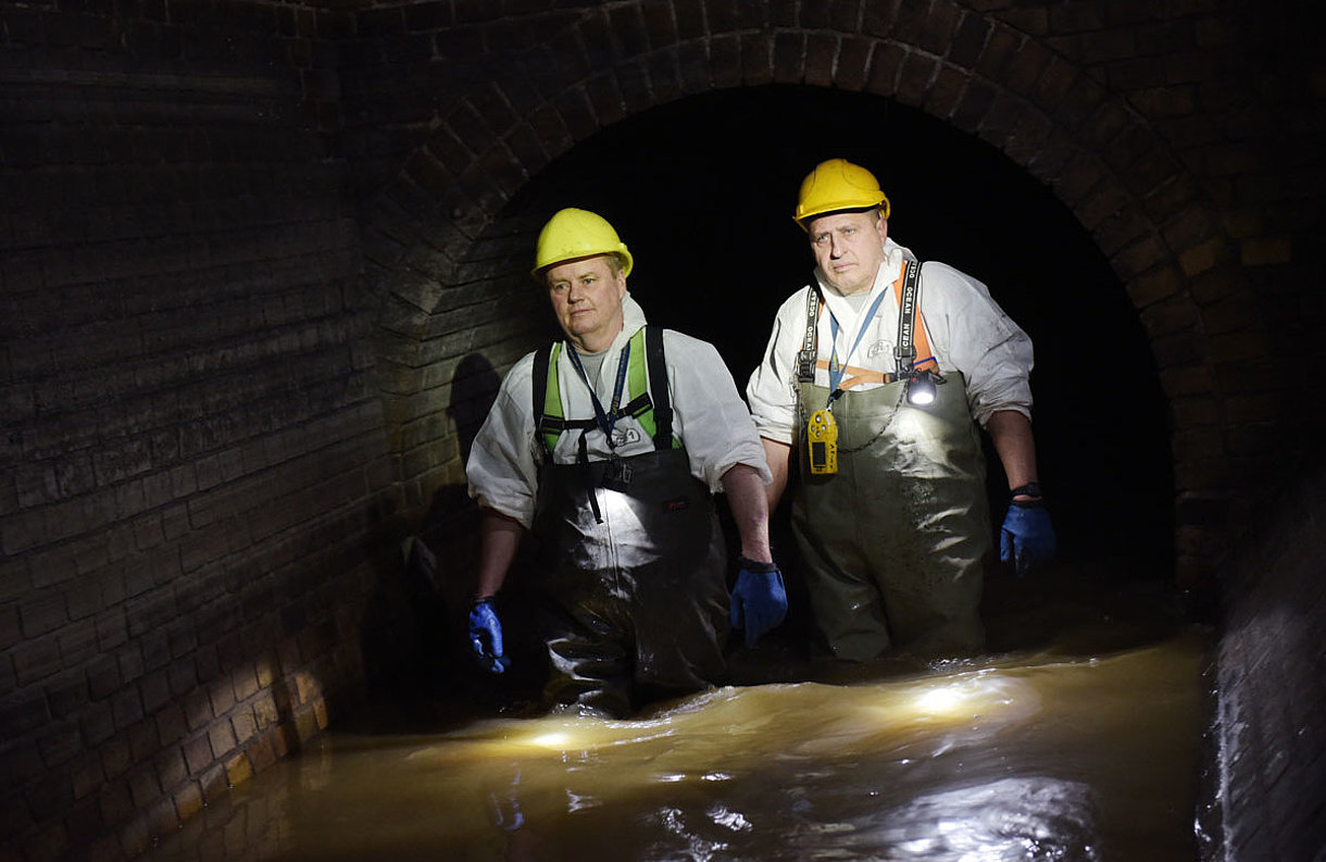Kontrollgang Abwasserkanal SWM Mitarbeiter Zwei Mitarbeiter von SWM aus dem Bereich Abwasser gehen durch Abwasser im Kanal