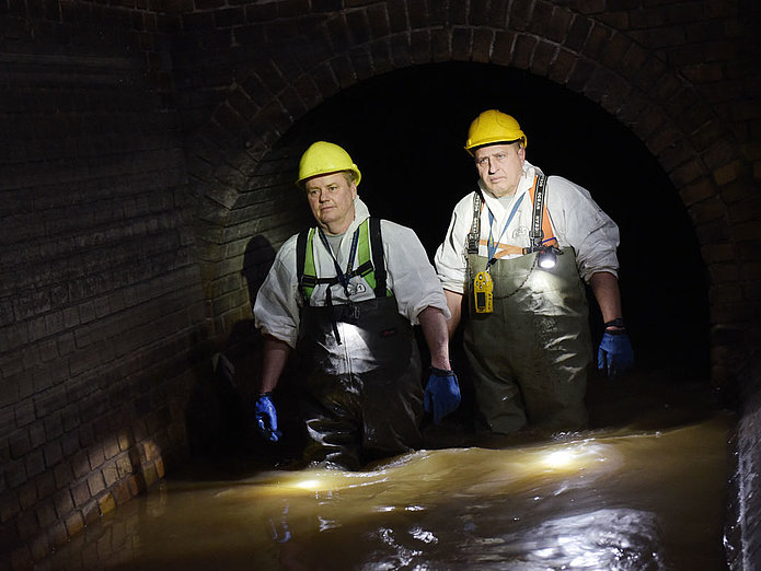 Zwei Mitarbeiter von SWM aus dem Bereich Abwasser gehen durch Abwasser im Kanal