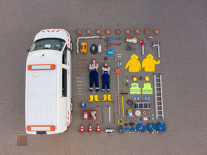 SWM Tetris Mitarbeiter aus dem technischen Bereich liegen nach dem Tetrisvorbild inkl. allem, was im Firmenwagen liegt, nebem dem Auto.