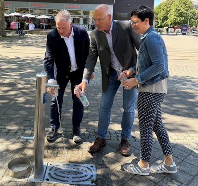 Zwei Männer und eine Frau der Einweihung eines Trinkwasserspenders