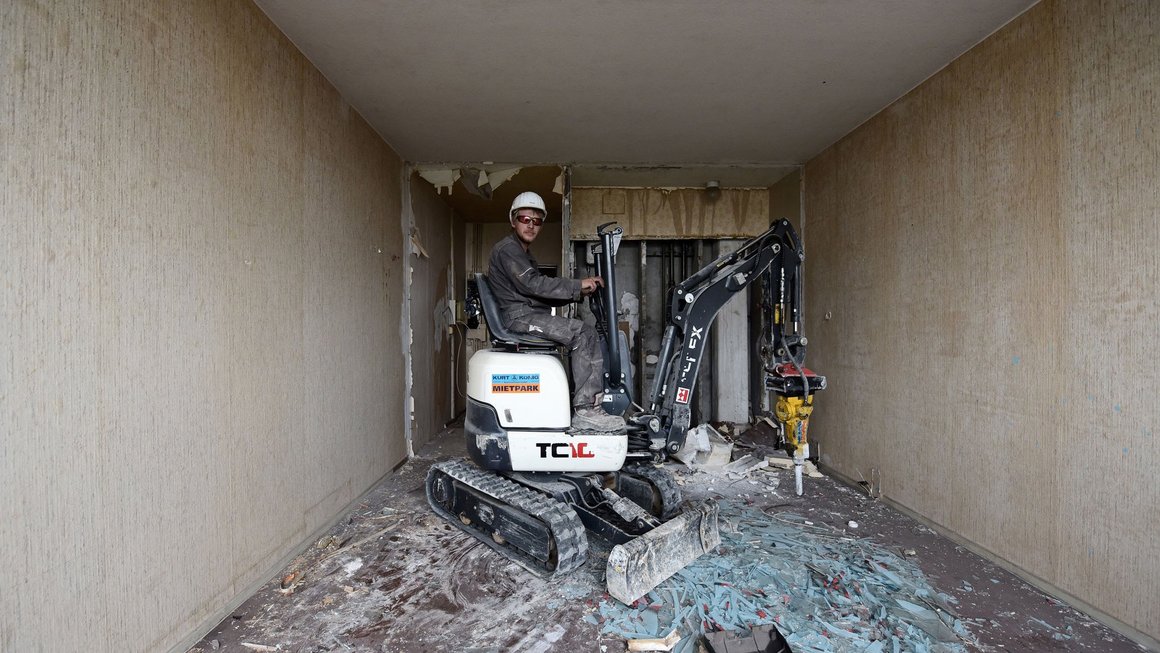 Bauarbeiter auf einem kleinen Abrissbagger in einer Wohnung Alte Blümchentapete im alten Blauen Bock