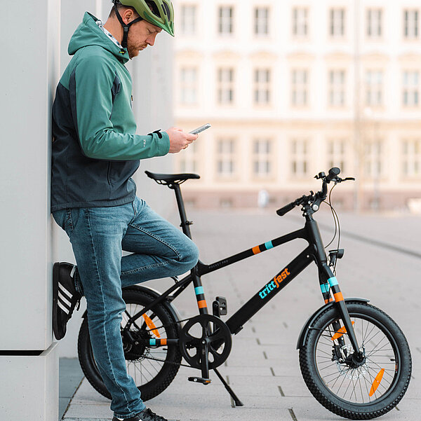 Radfahrer lehnt an Wand, neben ihm steht E-Bike E.mil