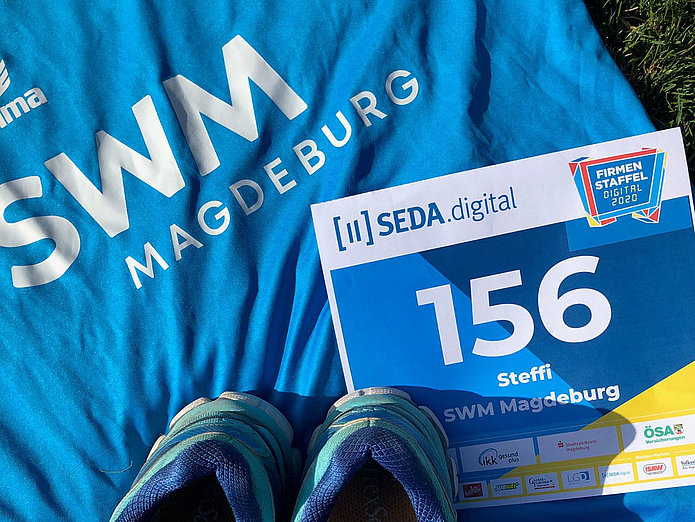 Teilnemer am digitalen Fimenstaffellauf SWM Laufshirt, Laufschuhe und Startnummer vom digitalen Firmenstaffellauf liegend auf dem Rasen