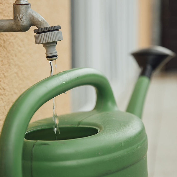 Wasser von einem Außenwasserhahn fliesst in eine grüne Gießkanne.