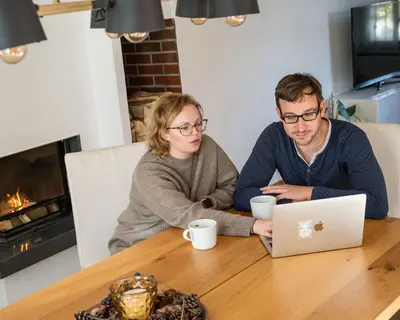 Ehepaar sitzt am Tisch und arbeitet gemeinsam am PC