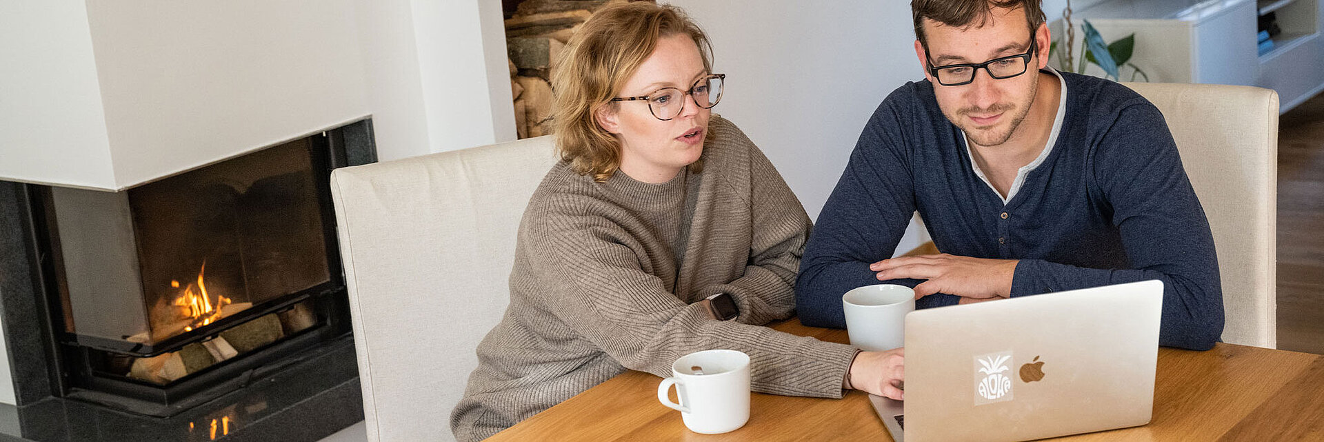 Ehepaar sitzt am Tisch und arbeitet gemeinsam am PC