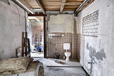Kernsanierung eines alten Hauses mit offenen Wänden und viel Baumaterial. Im Zentrum des Bildes ist eine Toilette zu sehen.