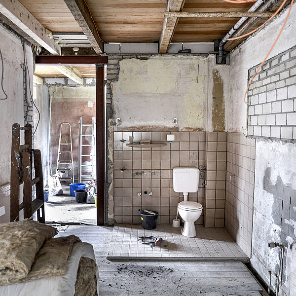 Kernsanierung eines alten Hauses mit offenen Wänden und viel Baumaterial. Im Zentrum des Bildes ist eine Toilette zu sehen. 