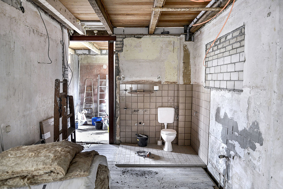 Kernsanierung eines alten Hauses mit offenen Wänden und viel Baumaterial. Im Zentrum des Bildes ist eine Toilette zu sehen.