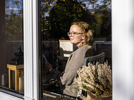 Frau sitzt im Haus und man blickt durch´s Fenster hinein