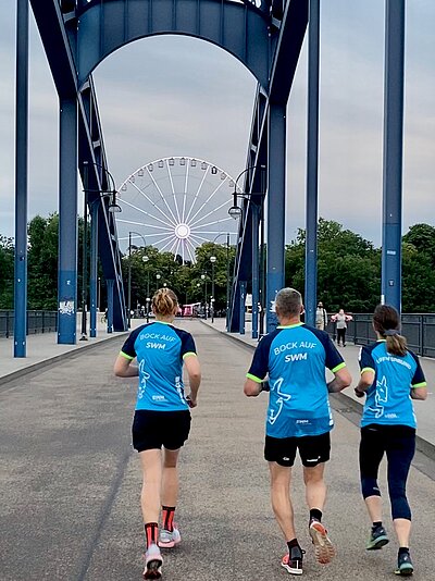 Drei SWM Mitarbeiter laufen im Firmen-T-Shirt über die Sternbrücke