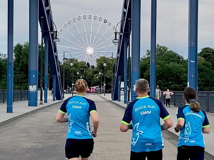 SWM Mitarbeiter laufen über die Sternbrücke Drei SWM Mitarbeiter laufen im Firmen-T-Shirt über die Sternbrücke