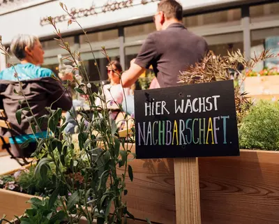 Blick in Nachbars Garten mit Schild "Hier wächst Nachbarschaft" im Vordergrund