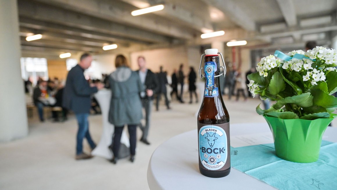 "Blauer Bock"-Bier auf einem Stehtisch neben Blumen beim Richtfest