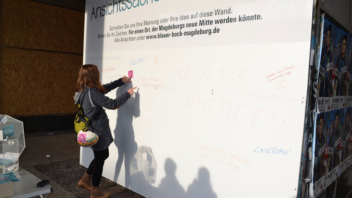 Frau liest Aufschriften an Plakatwand am alten Blauen Bock