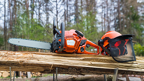 Motorsäge und Helm liegen auf einem Holzstamm