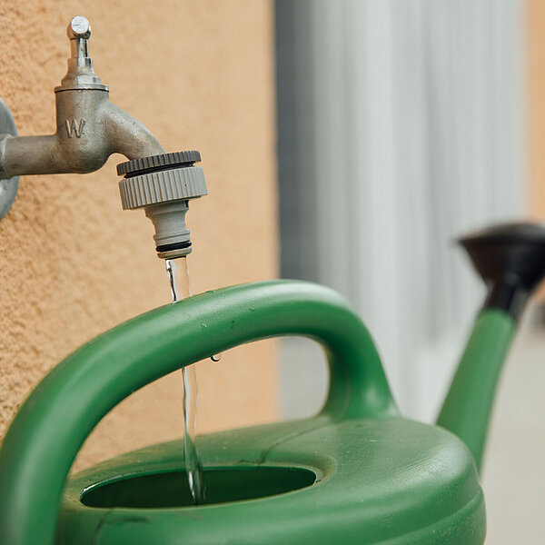 Wasser läuft in eine grüne Garten-Gießkanne