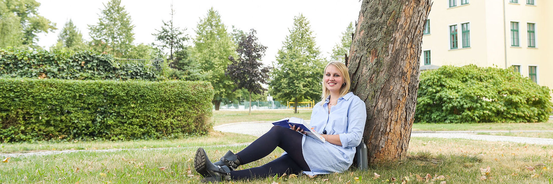 Studentin der dualen Ausbildung bei SWM sitzt auf dem Hochschul-Campus am Baum und liest