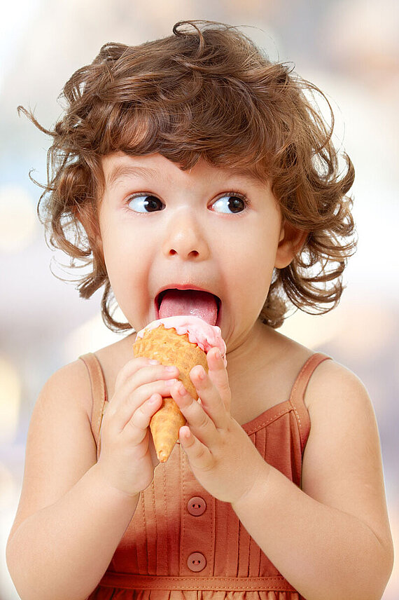 Kind leckt an einer Eiskugel in einer Eiswaffel und schaut dabei zur Seite.