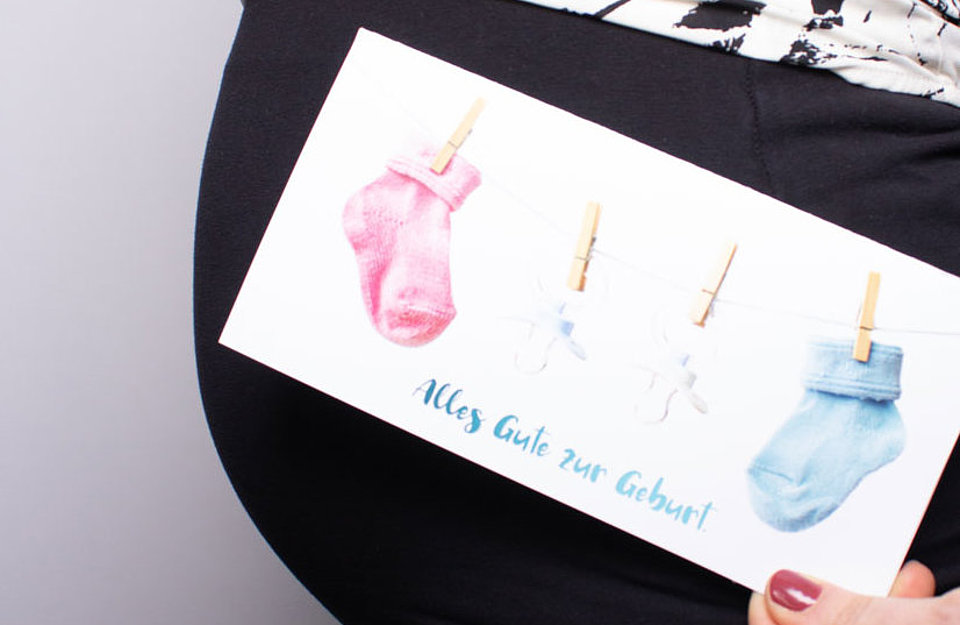 Geschenk zur Geburt Eine schwangere Frau hält die Glcükwunschakrte von SWM zur Geburt in die Kamera