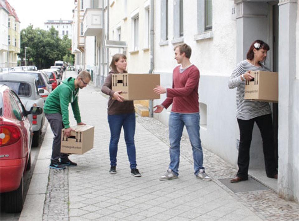 Vier junge Leute tragen Umzugskartons in ein Mehrfamilienhaus.