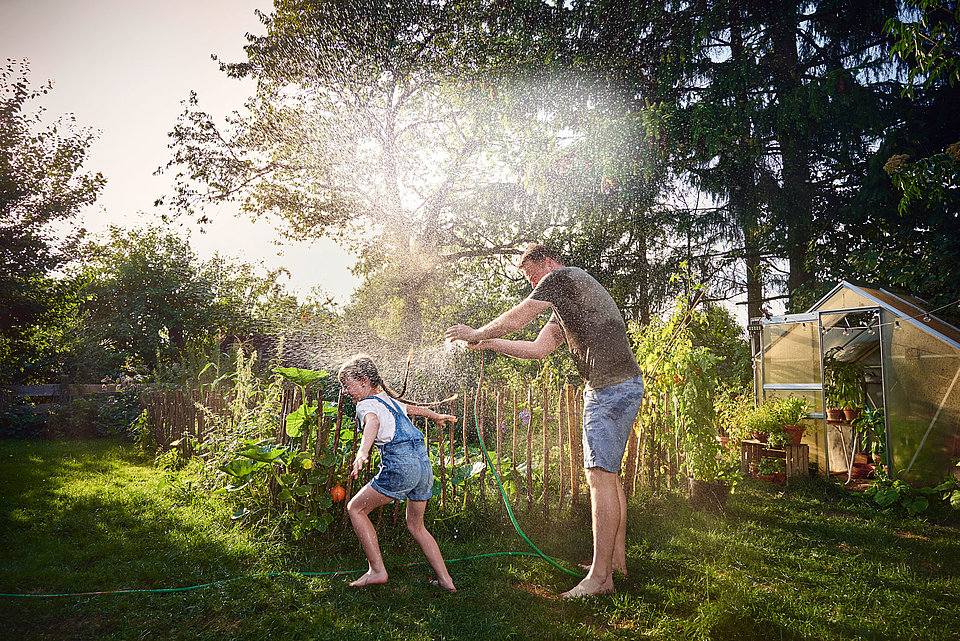 Vater und Kind spielen im Garten mit einem Wasserschlauch