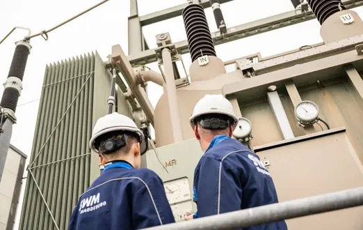 Zwei SWM Mitarbeiter:innen stehen vor technischen Anlage und blicken hoch