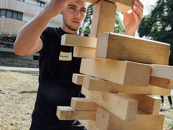 Azubi legt ein Stück Holz auf einen Holzturm