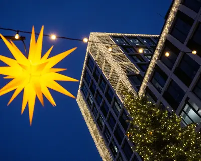 Gelber Herrnhuter Stern mit Blauen Bock mit Weihnachtsbeleuchtung im Hintergrund