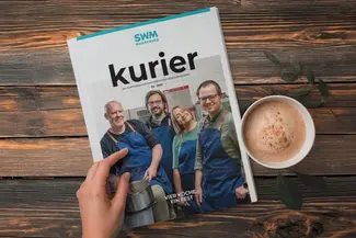 Die Ausgabe 02-2025 des SWM Kurier liegt auf einem Holztisch neben einer Kaffeetasse