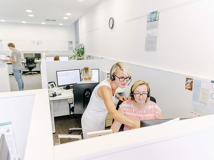 Eine SWM Mitarbeiterin zweig einer Kollegin im Callcenter etwas am Bildschirm