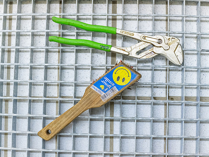 Werkzeug Zange und Bürste liegen auf einem Gitter