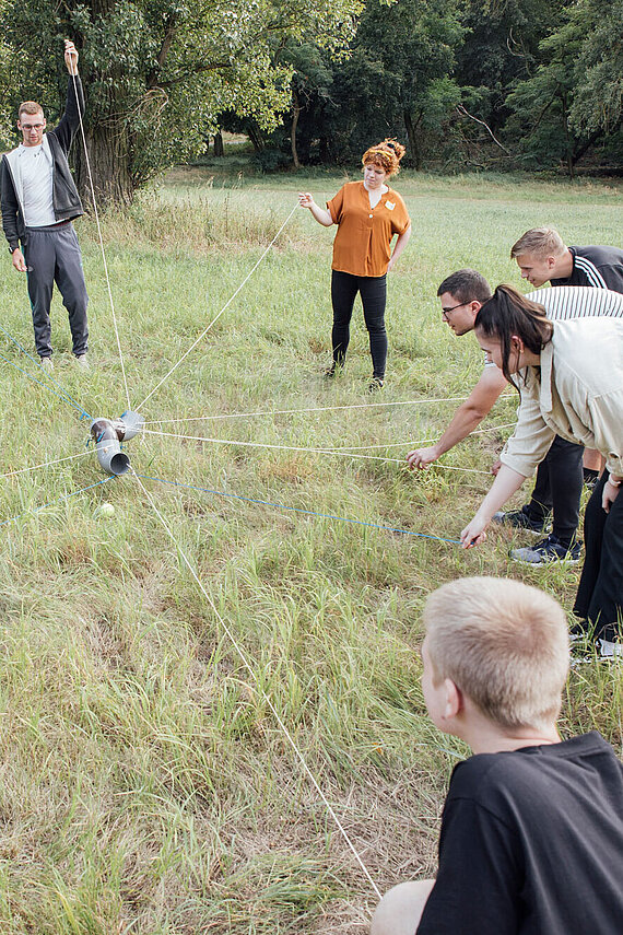 Azubis stehen auf der Wiese mit einer Rohrstrecke an vielen Schnüren