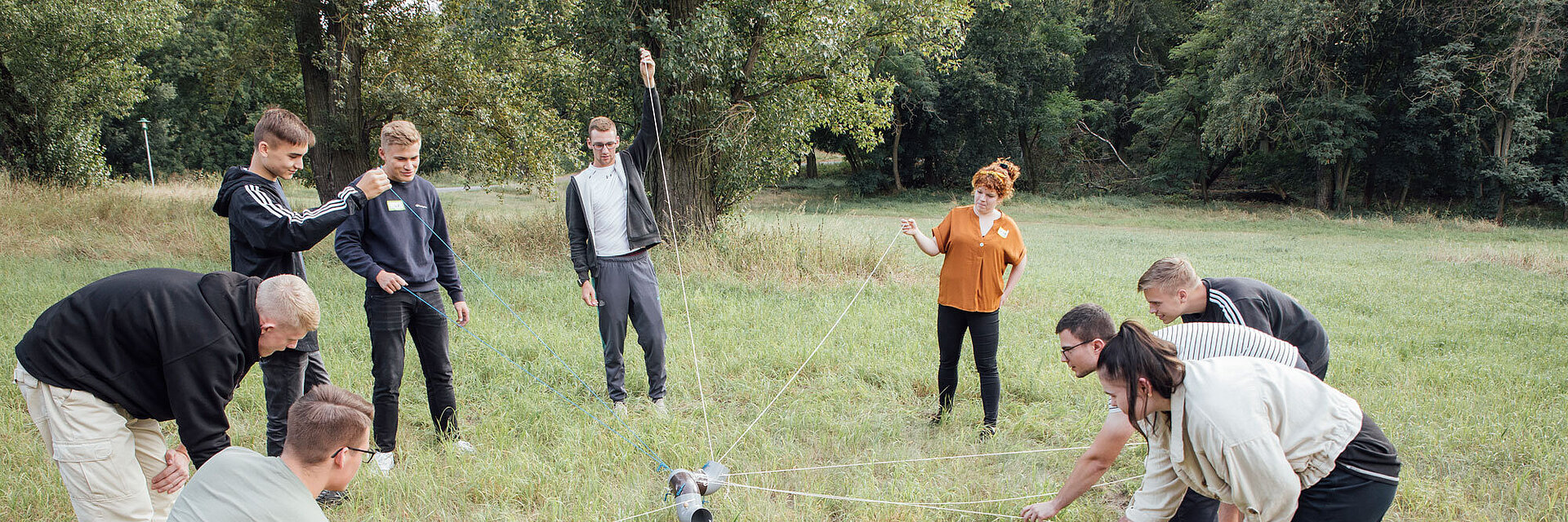 Azubis stehen auf der Wiese mit einer Rohrstrecke an vielen Schnüren