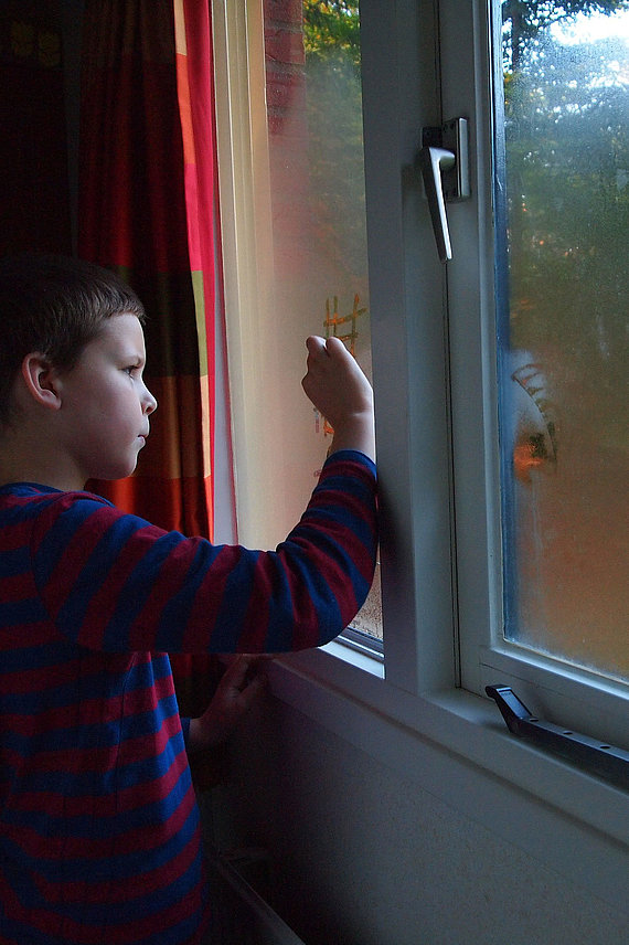 Junge malt auf beschlagene Fensterscheibe
