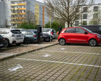 Blick auf einen Parkplatz mit E-Ladesäulen und einer Ladesäule tankt ein rotes Auto
