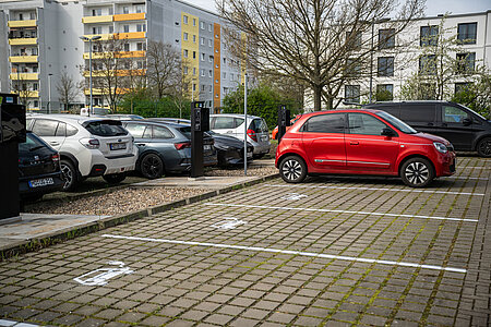 Blick auf einen Parkplatz mit E-Ladesäulen und einer Ladesäule tankt ein rotes Auto