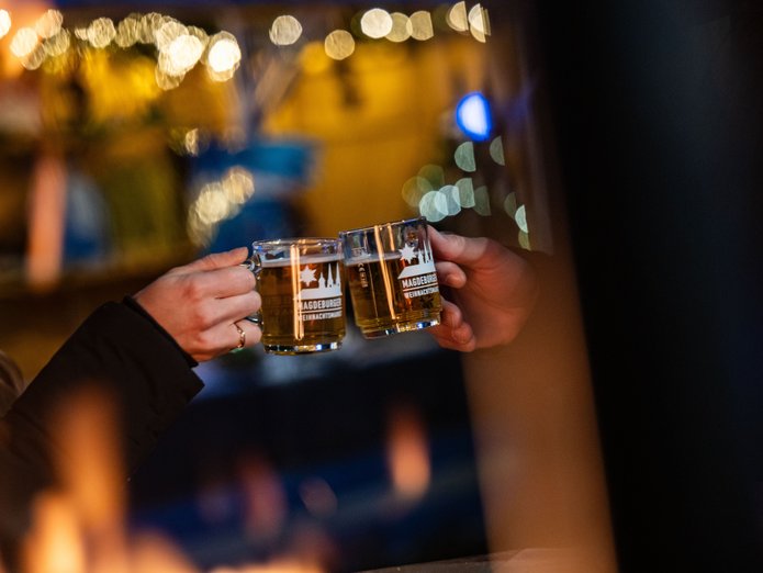 Glühweintassen auf dem SWM Weihnachtsmarkt Im dunkeln werden zwei Glühweingläser aneinandergehalten. Stimmungsvolles Licht ist im Hintergrund